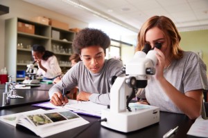 Two high school students work together with a book and microscope