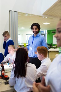 Teacher smiling as students work cheerfully on projects