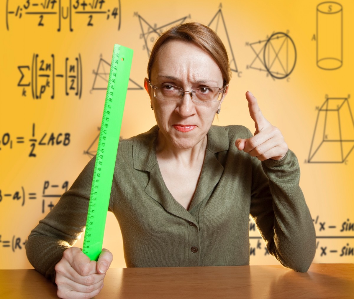 Stern looking teacher is pointing and weilding a brightly colored ruler.